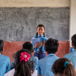 Une élève devant un tableau noir en train de faire la lecture à ses camarades de classe