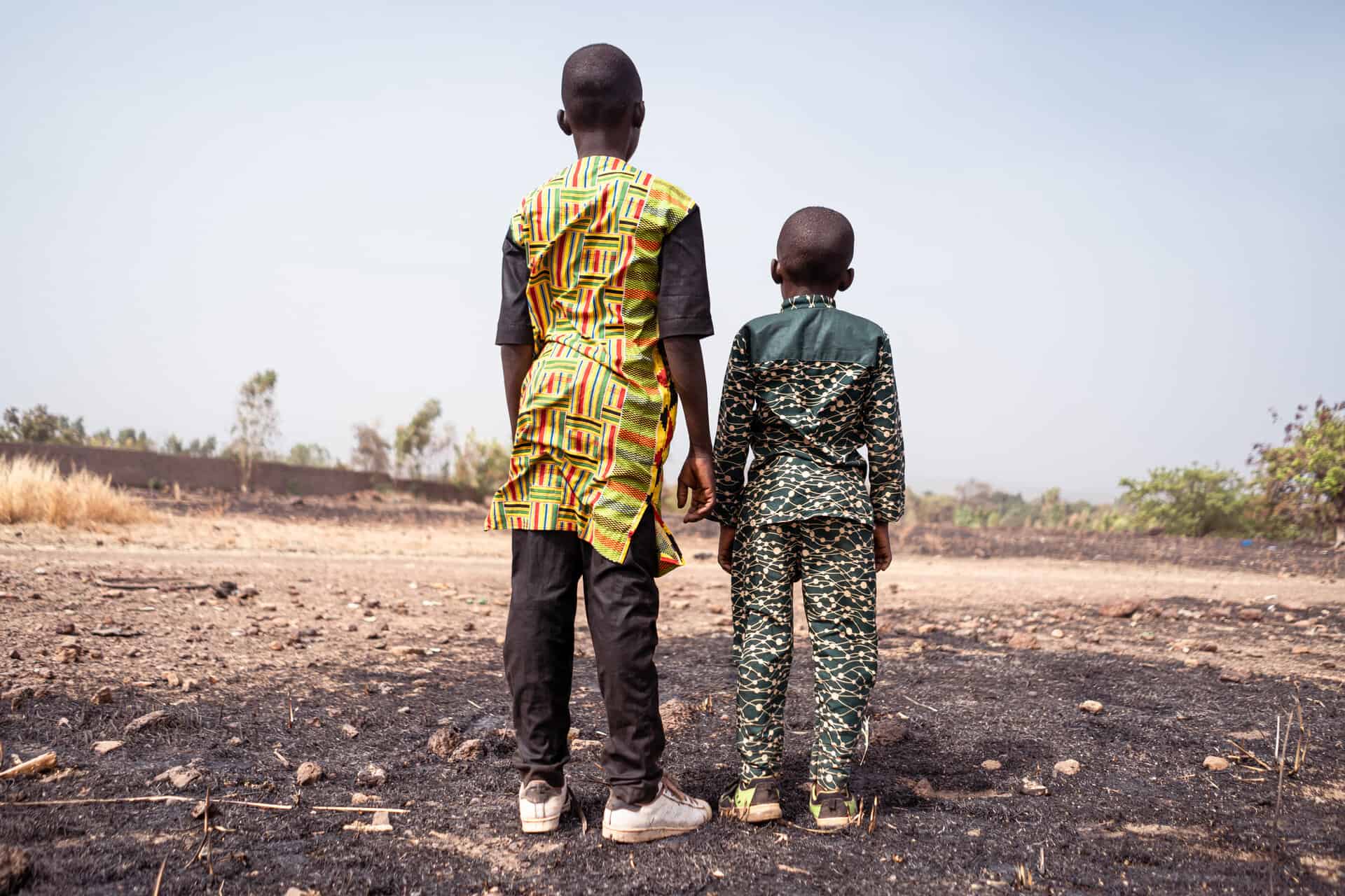 Two African children stand desperately in front of a burnt wheat field, a symbol of the climate crisis and global warming.